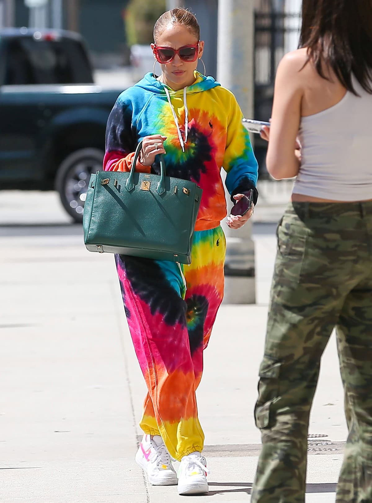 Jennifer Lopez glowed in Los Angeles on August 8, 2022, wearing a Polo Ralph Lauren eclipse shrunken tie-dye hoodie and sweatpants, Nike Air Force 1 sneakers, Jennifer Fisher silver thread hoop earrings, Quay chain reaction sunglasses, and a green Hermès Birkin bag