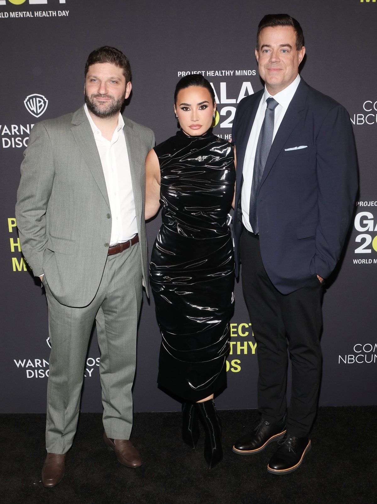 Despite standing in 4.5-inch Alexander McQueen Birdee boots, Demi Lovato appears notably petite between Michael D. Ratner and Carson Daly at the Project Healthy Minds World Mental Health Day Gala in New York City on October 10, 2024, wearing a sleek, ruched Alexander McQueen Fall 2024 jersey dress