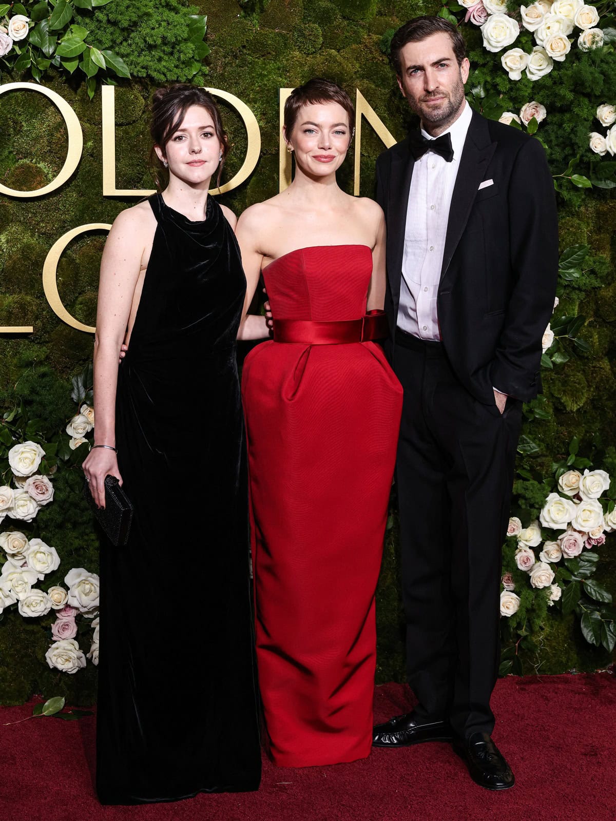 Emma Stone stuns in a custom Louis Vuitton ruby red silk bustier gown with a statement bow belt at the 2025 Golden Globe Awards, exuding timeless elegance alongside Ali Hertig in classic black velvet and Dave McCary in a sharp tuxedo