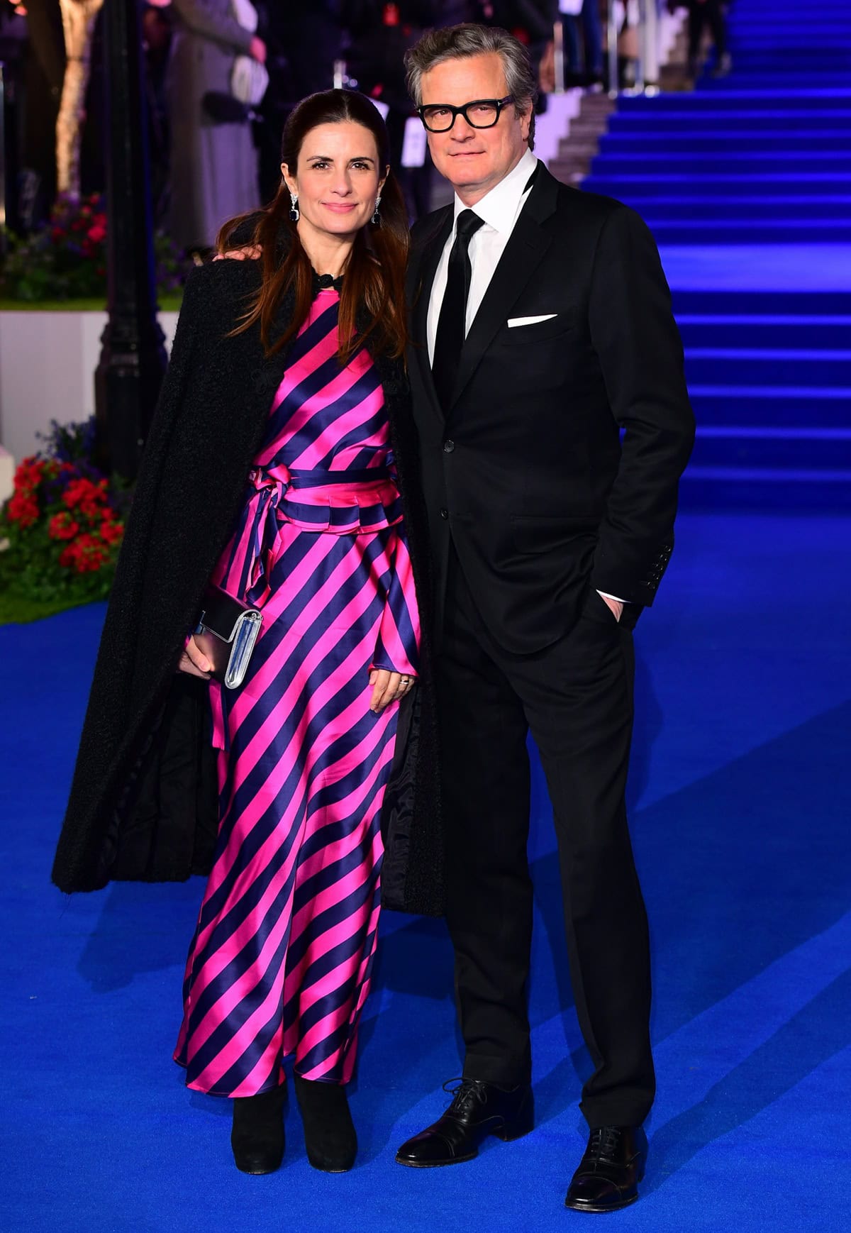 Livia Giuggioli stuns in a vibrant pink-and-purple striped gown, complemented by a black coat, as she attends the "Mary Poppins Returns" European premiere with Colin Firth at the Royal Albert Hall in London on December 12, 2018