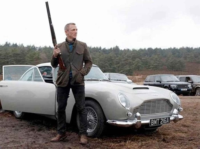 James Bond wearing a Barbour Beacon Heritage sports jacket while cruising up to the Scottish Highlands in a silver 1965 Aston Martin DB5