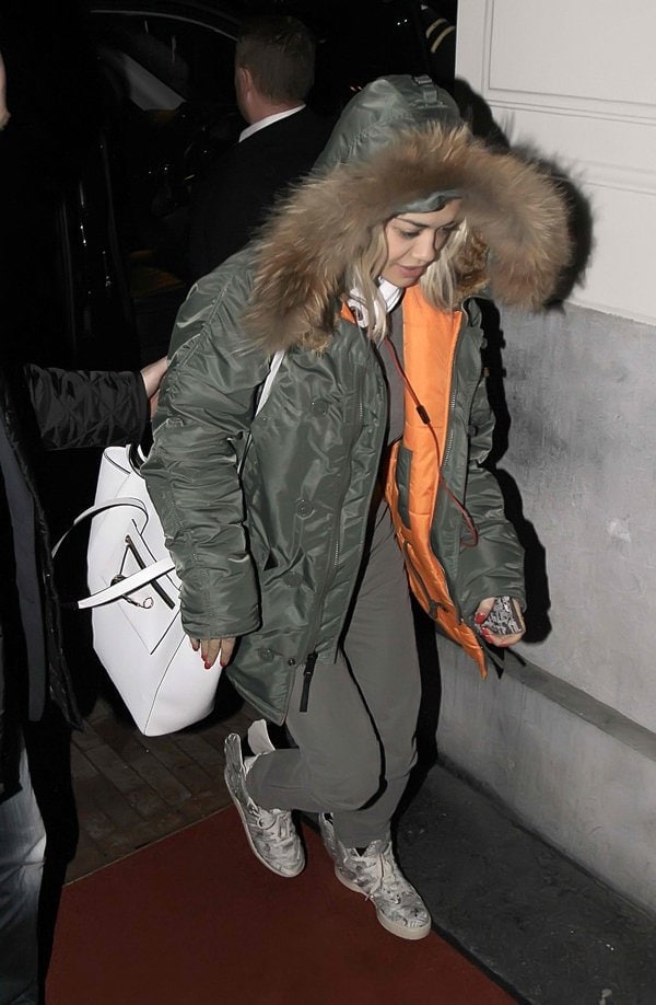 Rita Ora looked fresh-faced and cozy in denim overalls and a dark green parka with large fur trim, accessorizing with a white handbag and matching Beats By Dre headphones