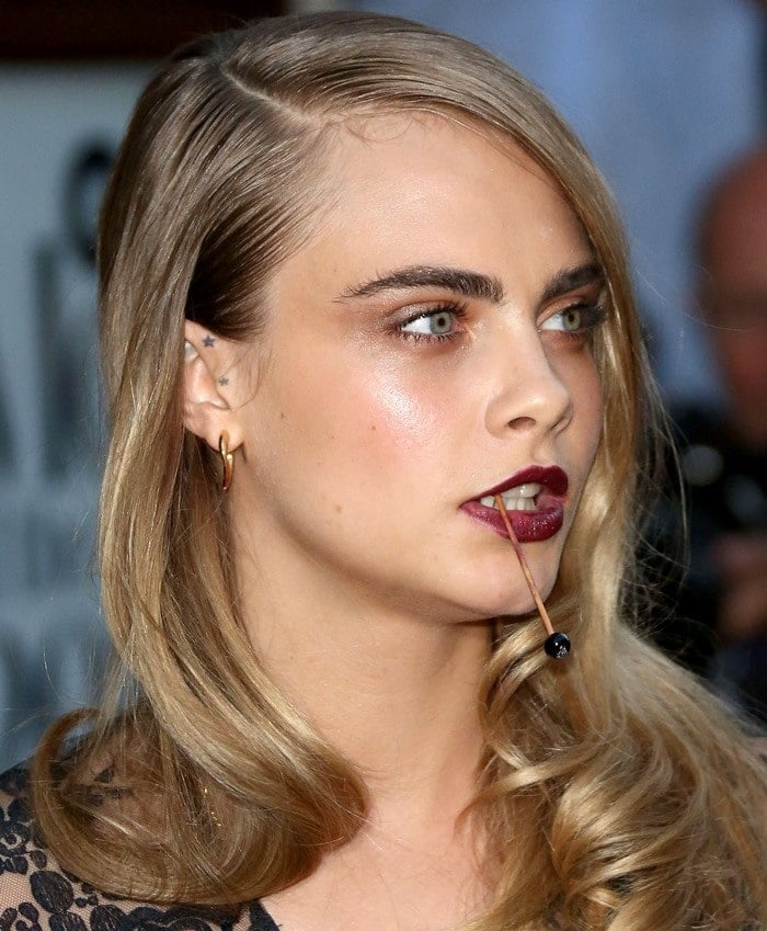 Cara Delevingne's unique vampire-esque makeup and intriguing mouth accessory add a mysterious touch to her look, perfectly complementing her Burberry Prorsum ensemble
