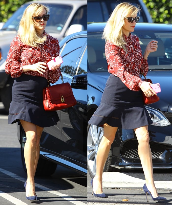 Reese Witherspoon showing her toned legs in a short black skirt paired with a red patterned blouse