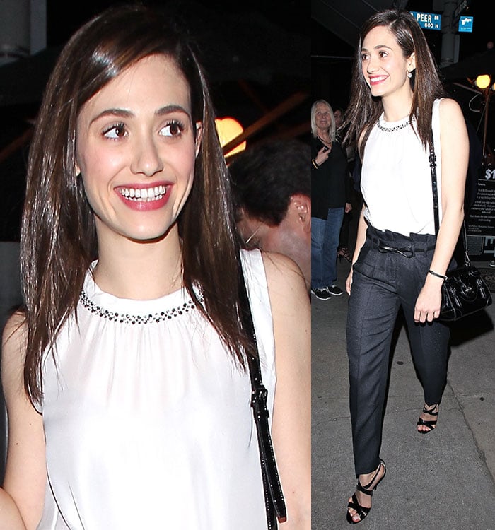 Emmy Rossum in a white sleeveless blouse tucked into high-waist black pants