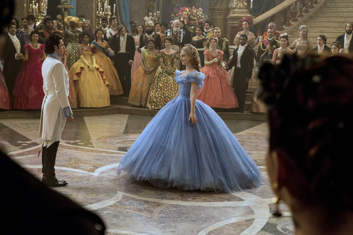 Lily James, as Cinderella, enchants the ballroom with her tiny waist accentuated by a corset and a voluminous blue gown