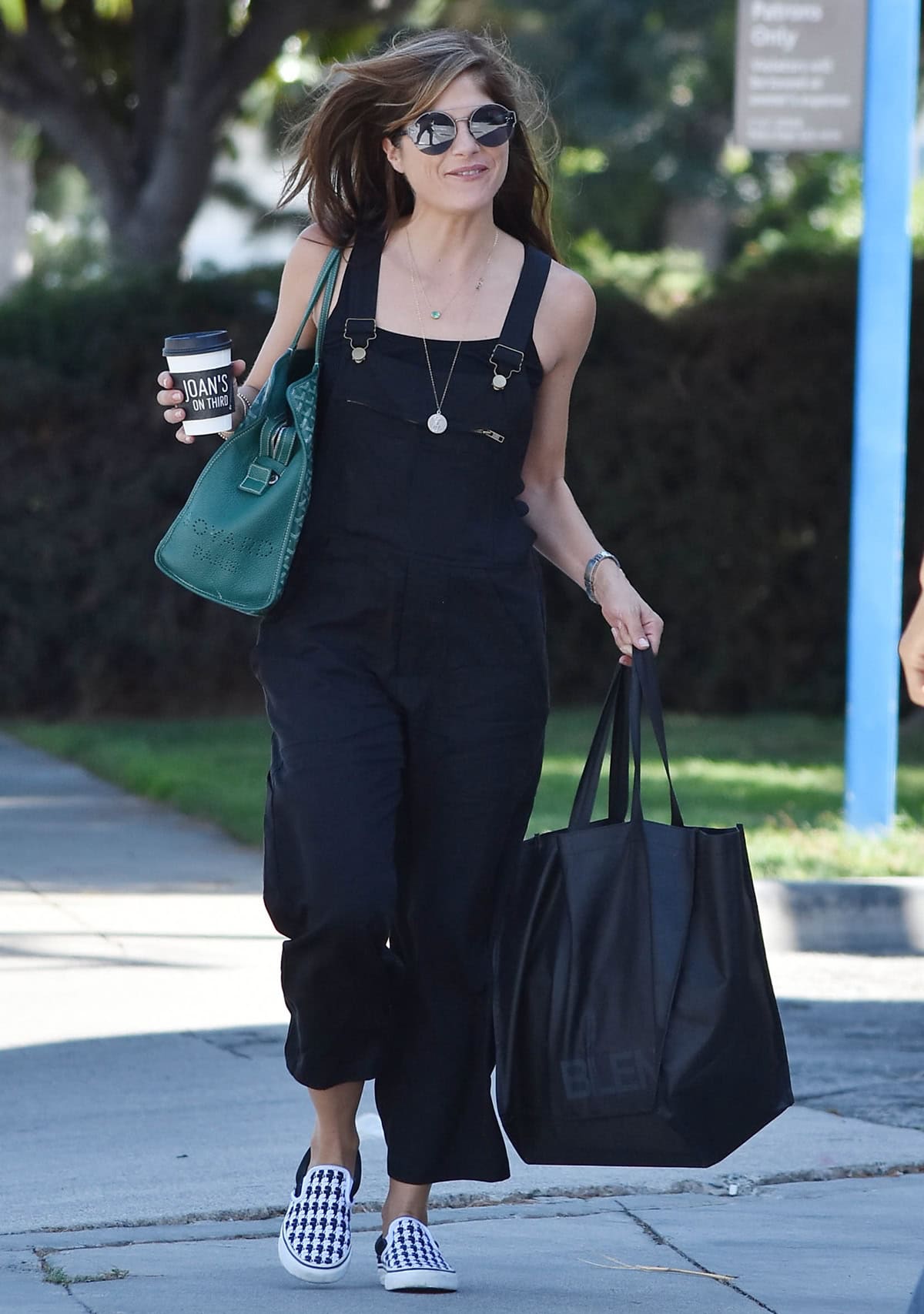 Selma Blair looks effortlessly chic running errands in black overalls paired with houndstooth slip-on sneakers and a green tote bag