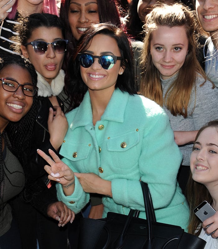 Demi Lovato flashes a peace sign as she poses with fans outside of Kiss FM and Capital Radio studios