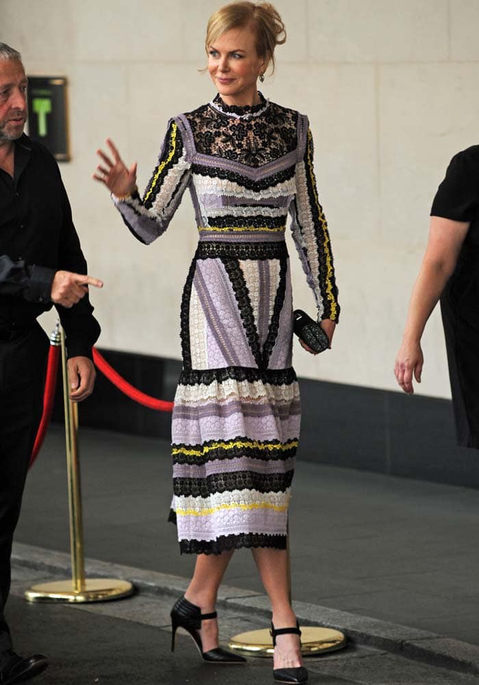 Nicole Kidman smiles and waves while wearing a purple, black, white and yellow frock from Erdem