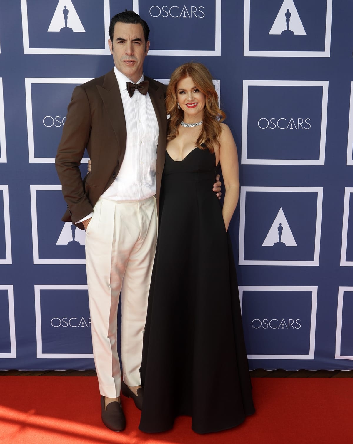 Isla Fisher in a black low-cut Dior gown and her husband Sacha Baron Cohen attend a screening of the Oscars