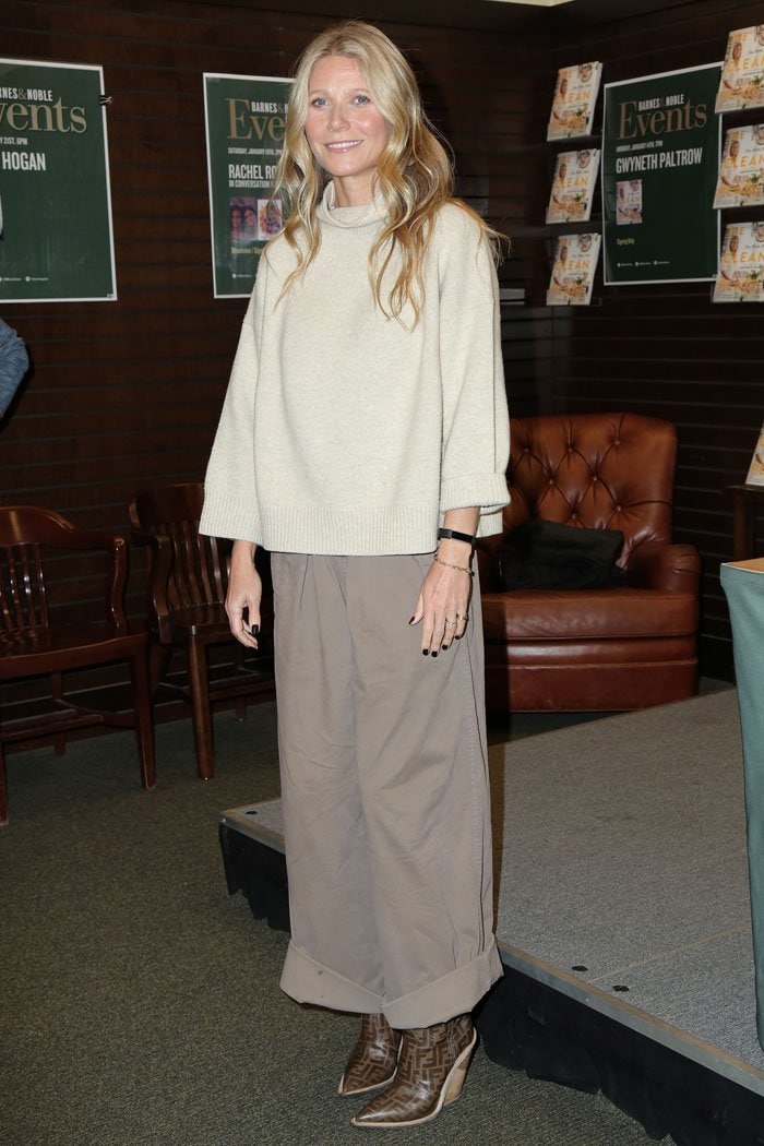 Gwyneth Paltrow in a frumpy brown outfit consisting of a loose beige turtleneck sweater, wide-leg pleat-front pants, and Fendi logo-print cowboy boots