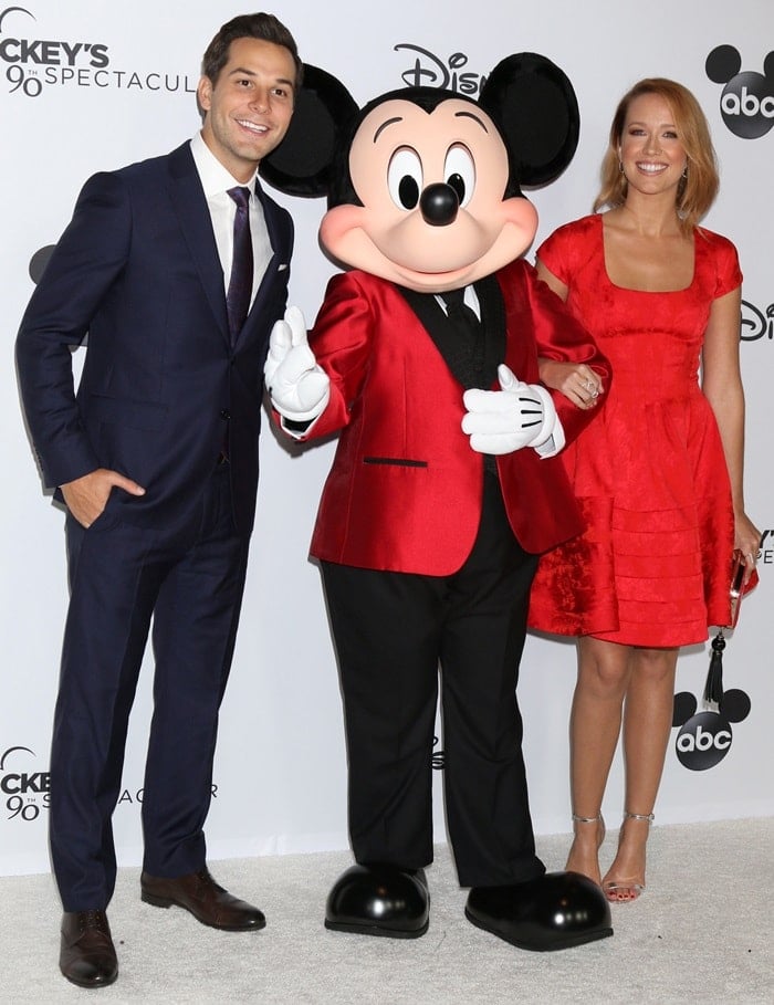 Anna Camp shines in a vibrant red dress alongside Skylar Astin and Mickey Mouse at Mickey’s 90th Spectacular celebration