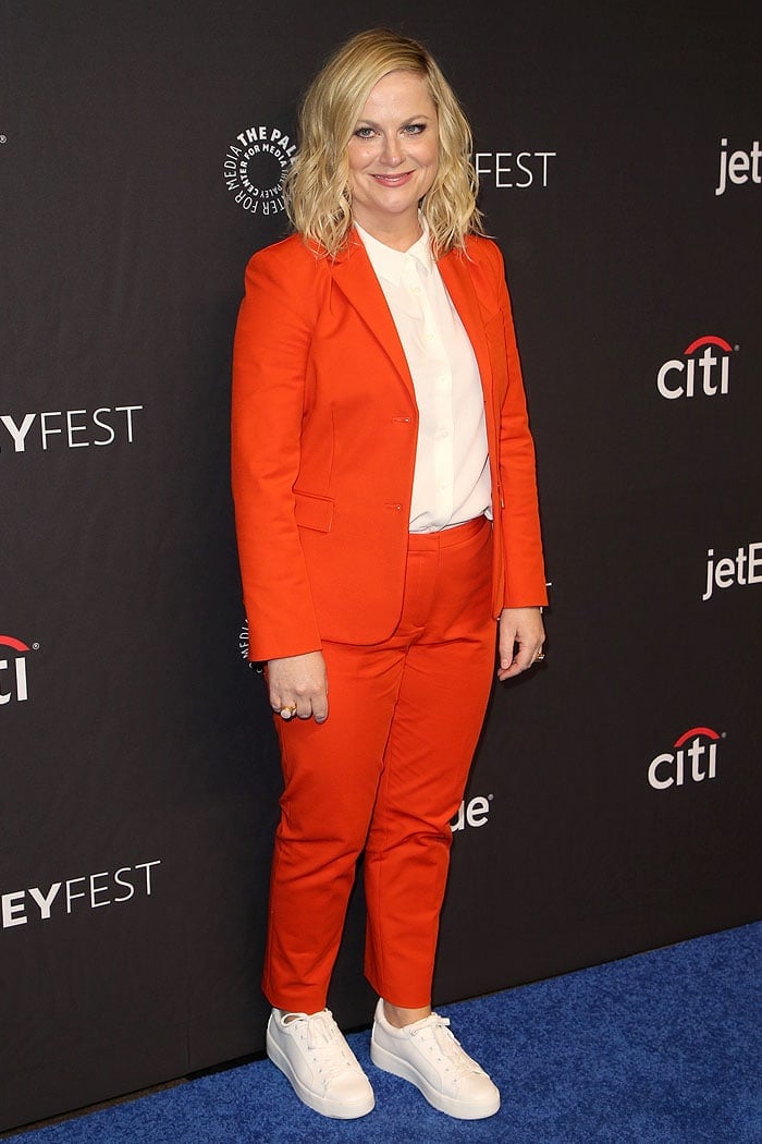 Amy Poehler in an orange pantsuit and white sneakers