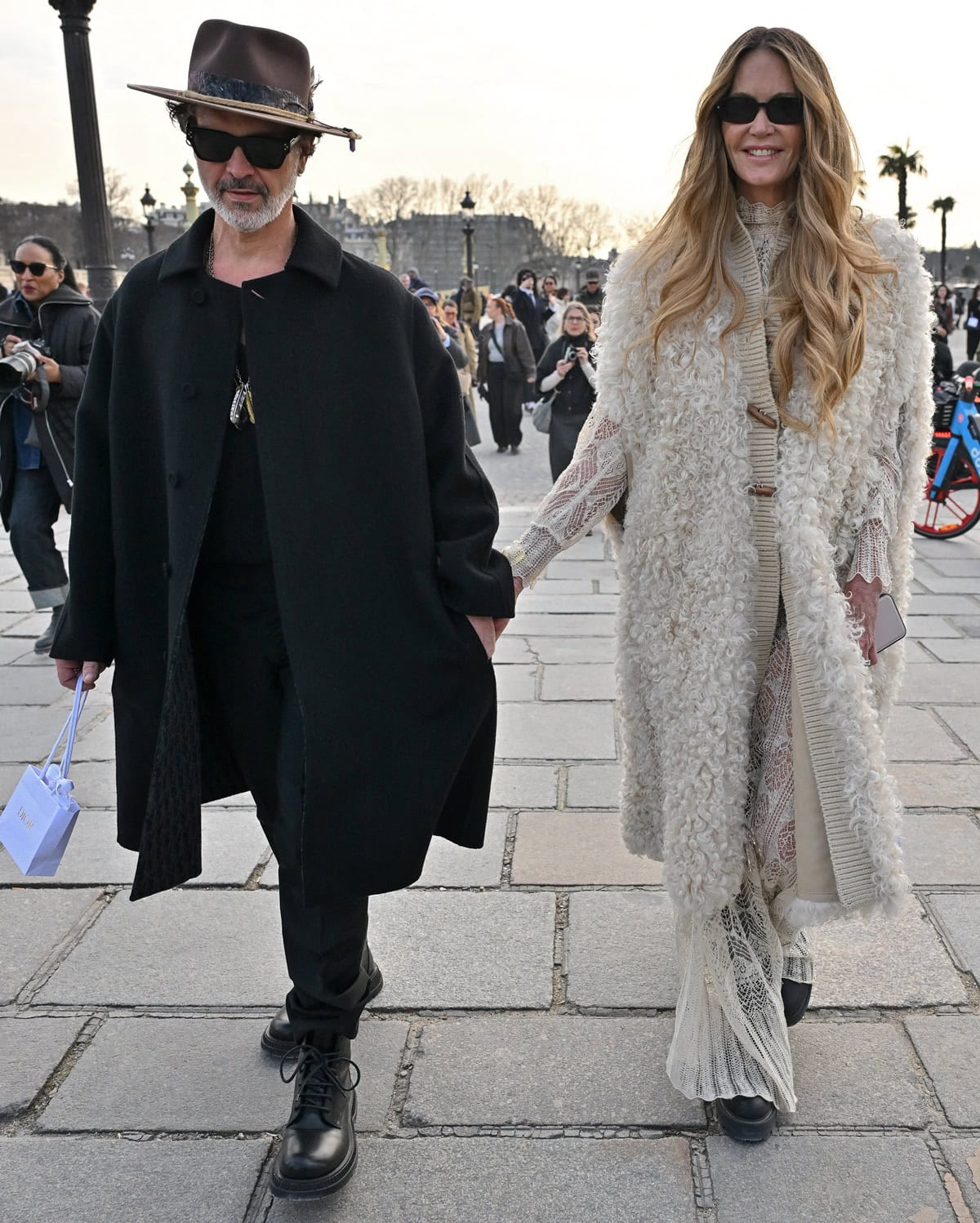 Elle Macpherson, towering over Doyle Bramhall, exudes bohemian elegance in a textured shearling coat and lace ensemble at the Christian Dior show during Paris Fashion Week on March 4, 2025