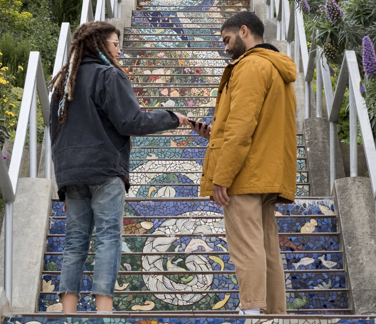 Zendaya embraces a laid-back, edgy look in The OA, wearing distressed cropped jeans, a dark oversized jacket, and her signature dreadlocks with blue highlights