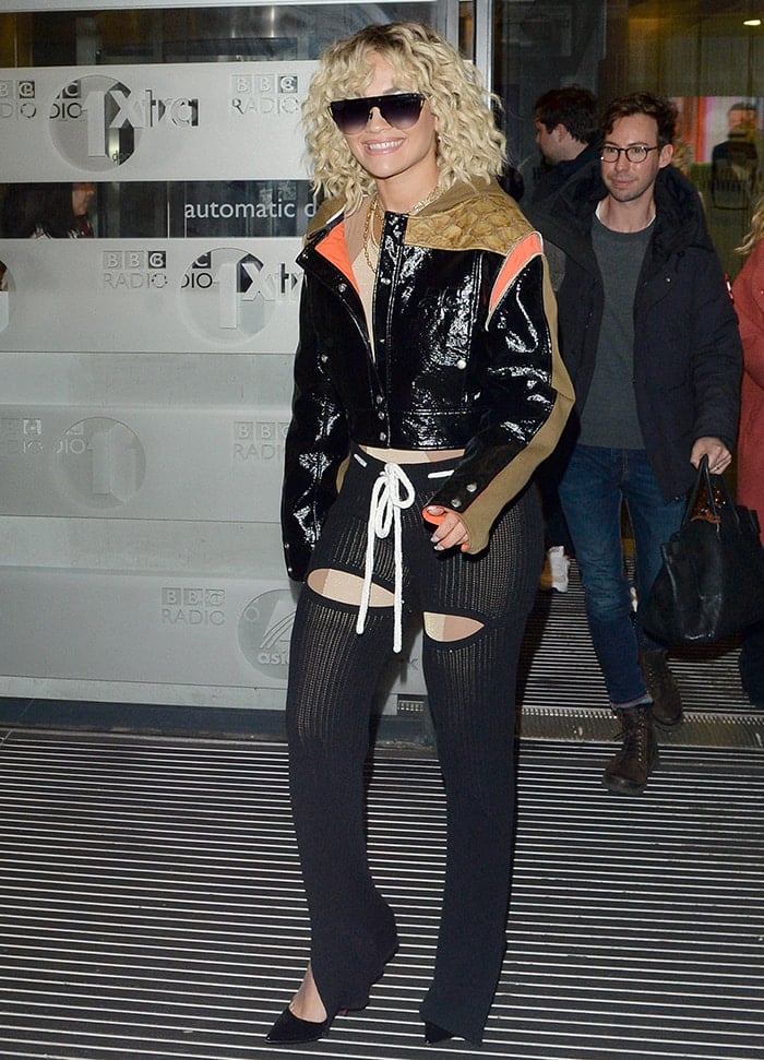 Rita Ora in skintight jumpsuit worn underneath a leather jacket and rib-knit trousers