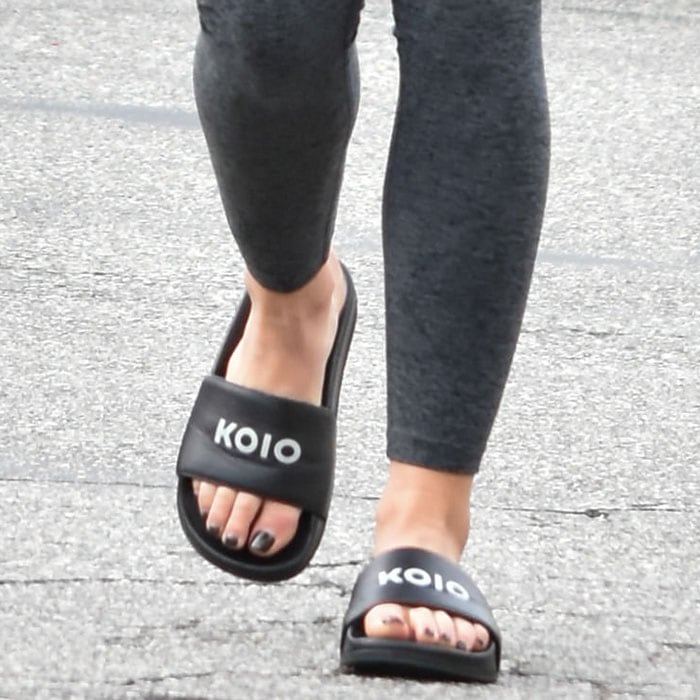 Lucy Hale wearing a pair of black Koio slide sandals that show off her black pedicure