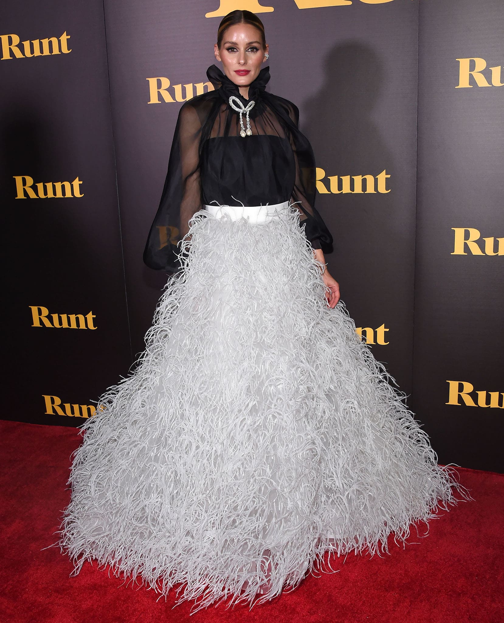 Olivia Palermo steals the spotlight in a two-piece Monique Lhuillier Spring 2022 look featuring a black sheer blouse and a white feathered ball gown skirt