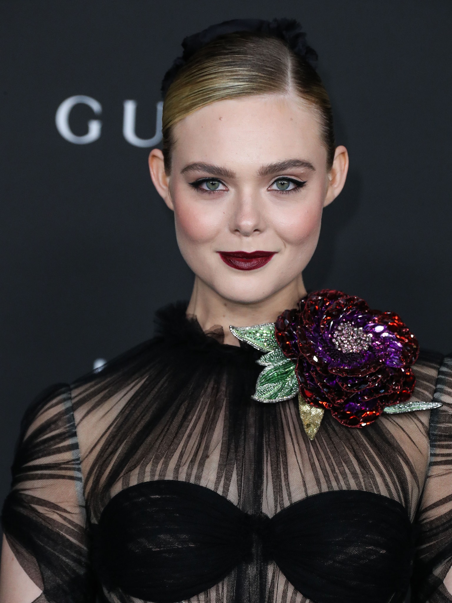 Elle Fanning wears tight hair bun and glams up further with winged eyeliner and a swipe of burgundy lipstick