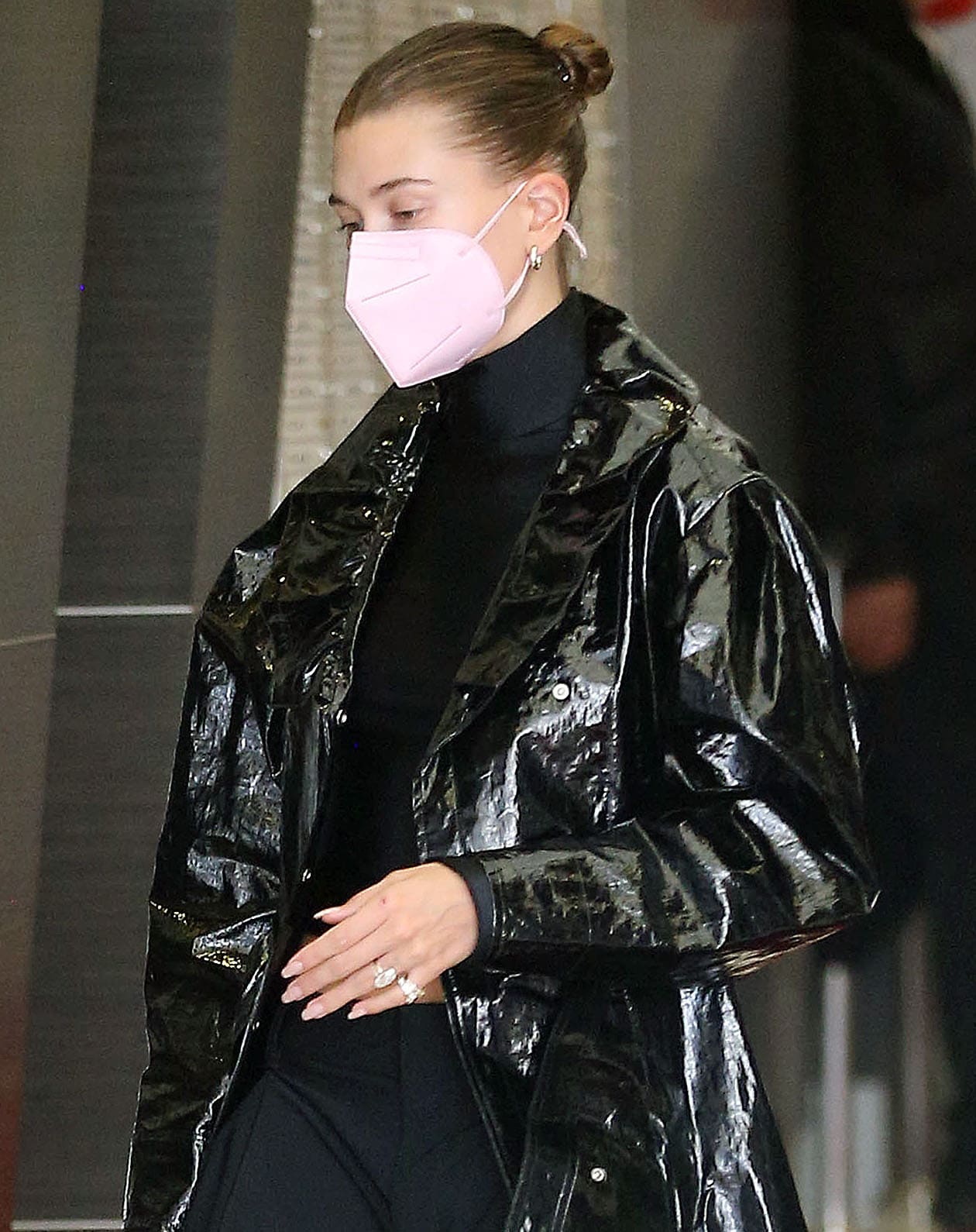 Hailey Bieber styles her all-black outfit with minimal jewelry and a pink face mask