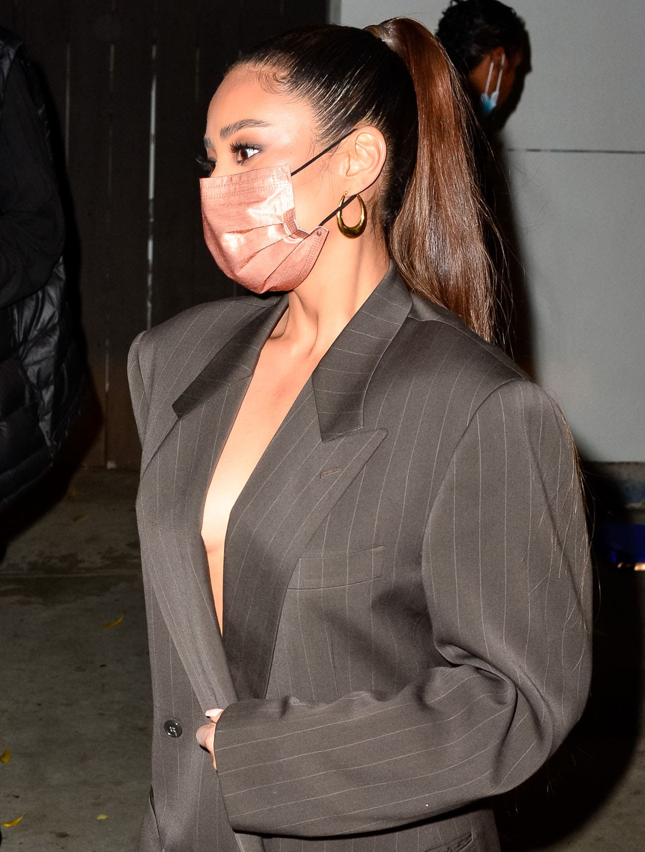 Shay Mitchell exudes sleek elegance in an oversized gray pinstripe blazer complemented by gold hoop earrings and a rose gold fabric face mask