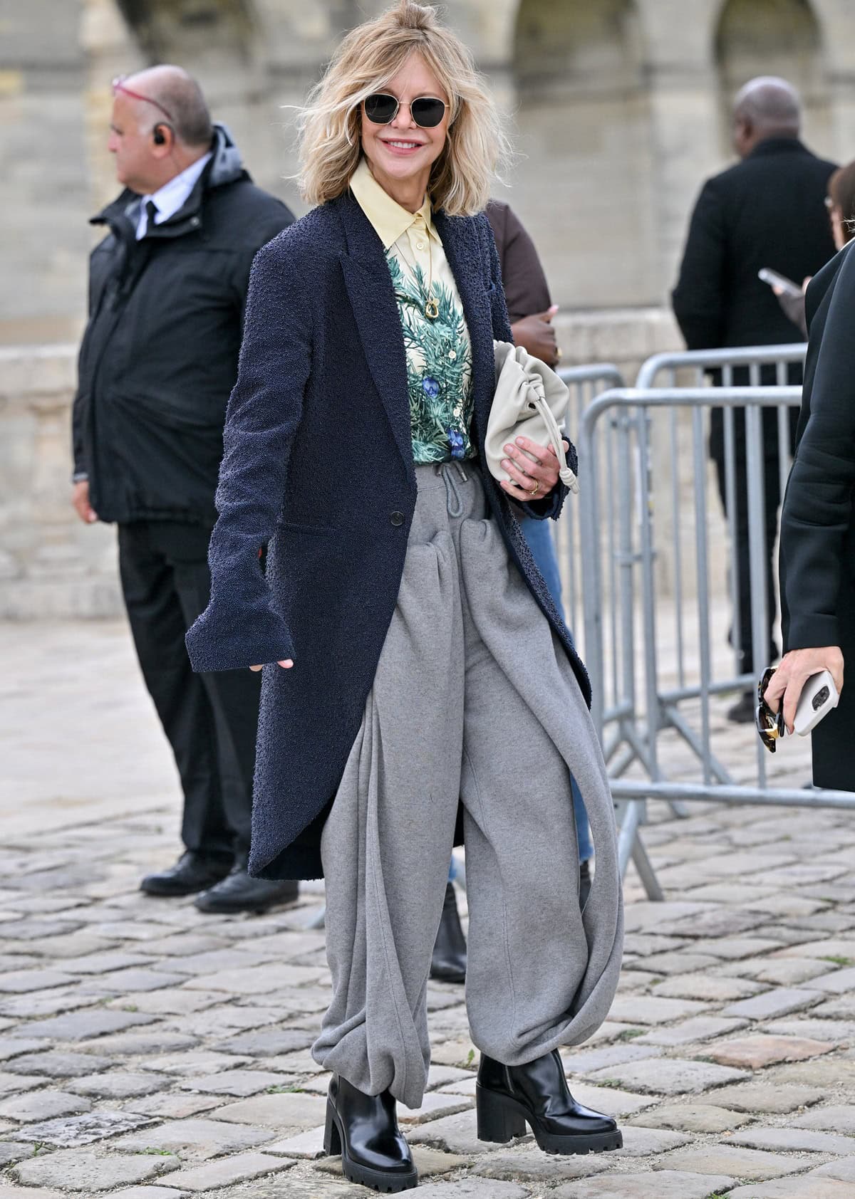 Meg Ryan exudes effortless fall chic at Loewe's Paris Fashion Week show in a navy beaded blazer, artful printed shirt, gray sculptural trousers, and chunky black platform boots on September 27, 2024