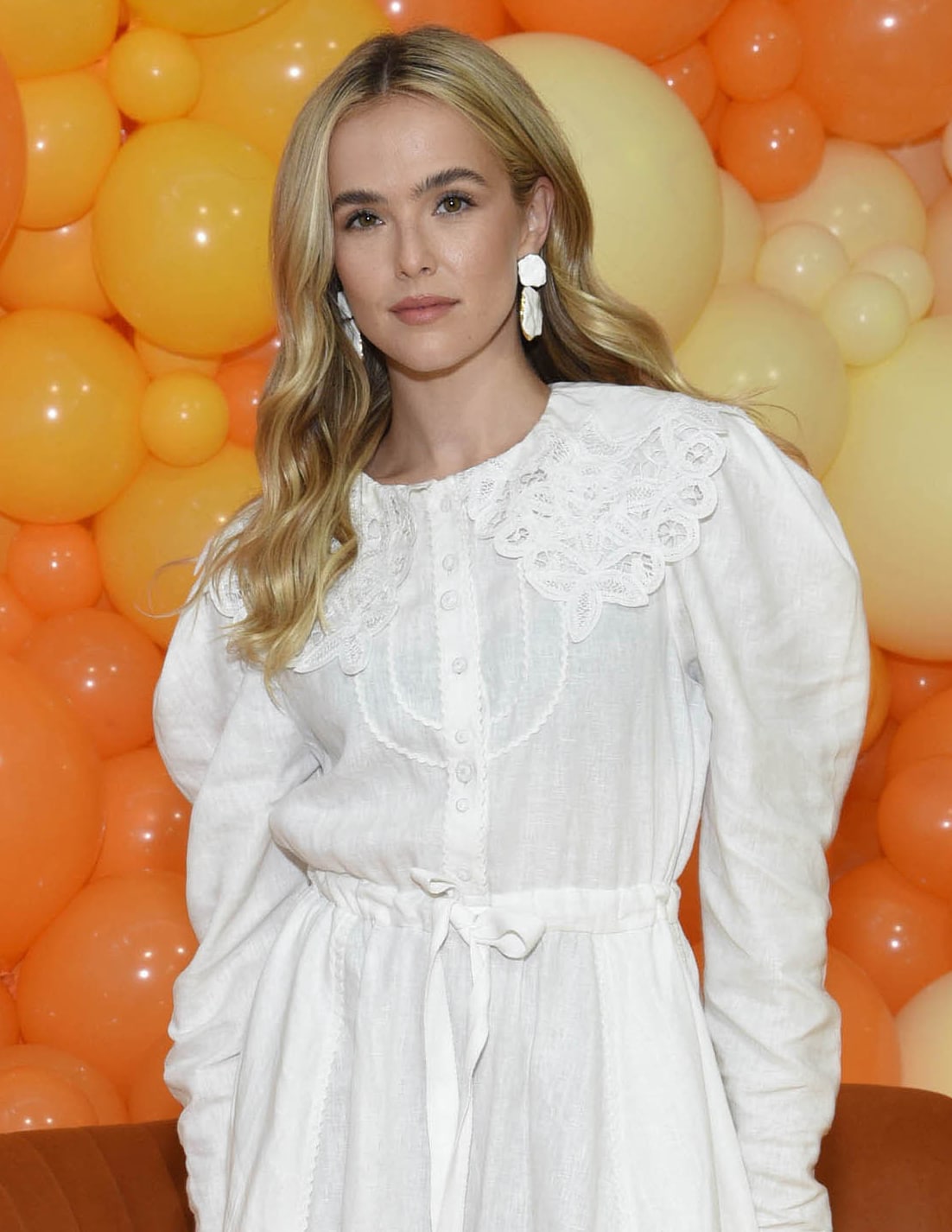 Zoey Deutch styles her hair in loose waves with one side tucked behind her ear, showcasing her Joanna Laura Constantine white enamel earrings