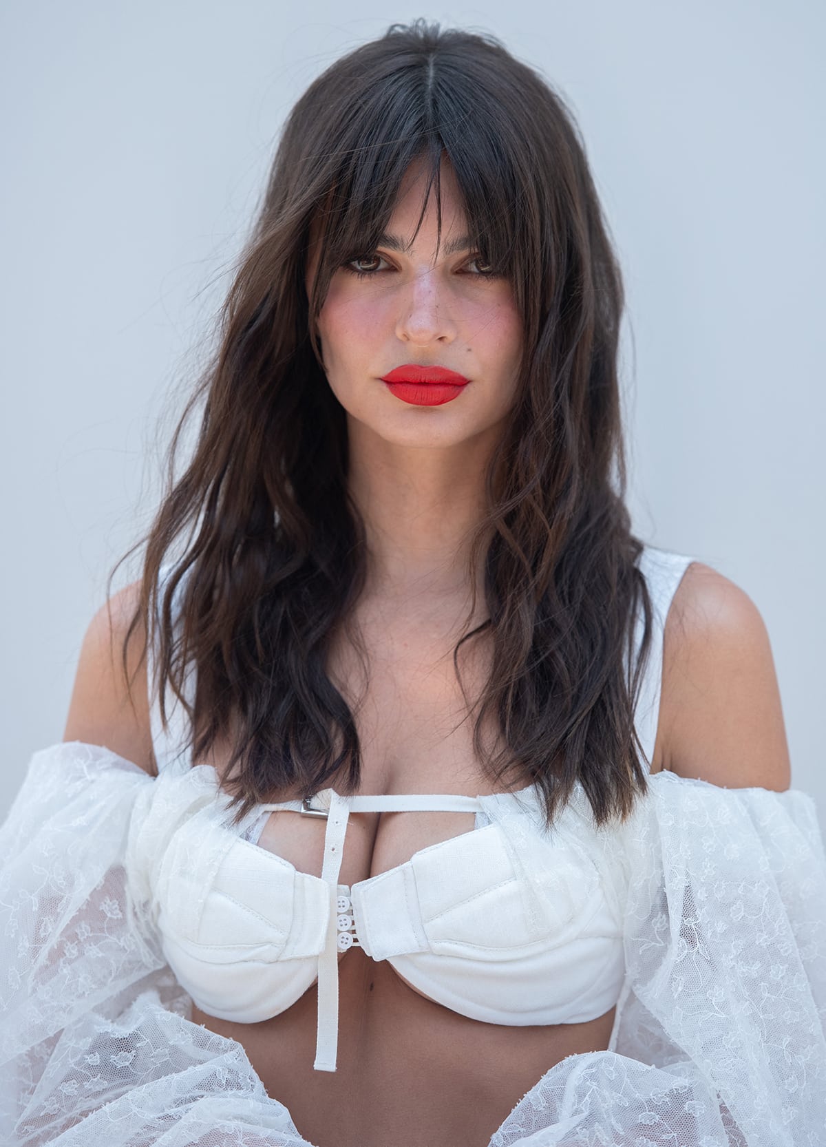 Emily Ratajkowski wears sultry messy waves and adds a splash of color to her angelic all-white ensemble with bright red lipstick