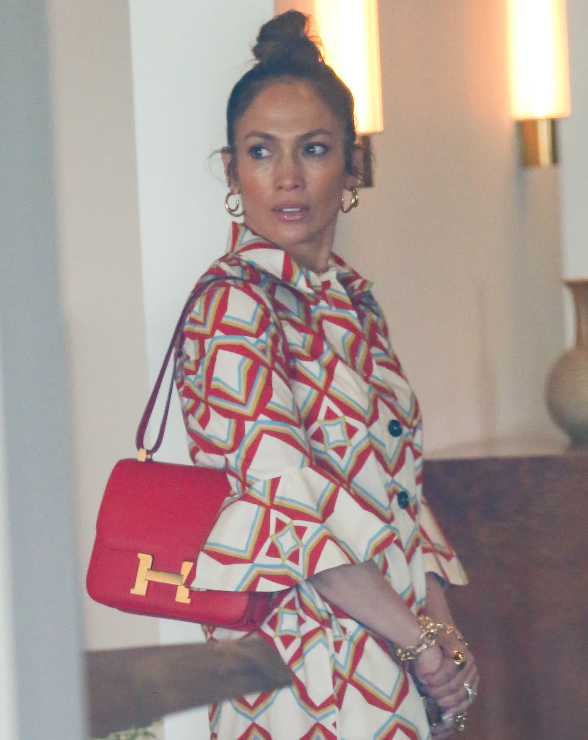 Jennifer Lopez wears a messy topknot and ties her look together with gold jewelry and a red Hermes bag