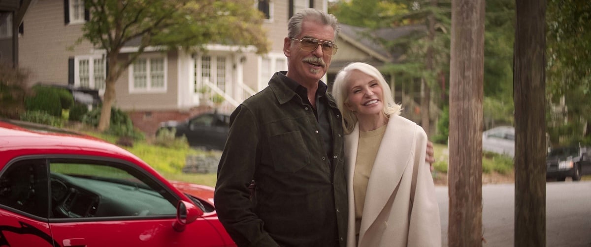 Pierce Brosnan towers over Ellen Barkin as they stand close together in the 2023 action-comedy film The Out-Laws