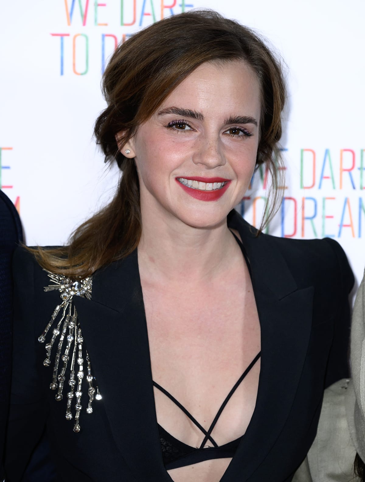 Emma Watson ties her hair back into a messy ponytail and sports bold red lip color for a sultry finish