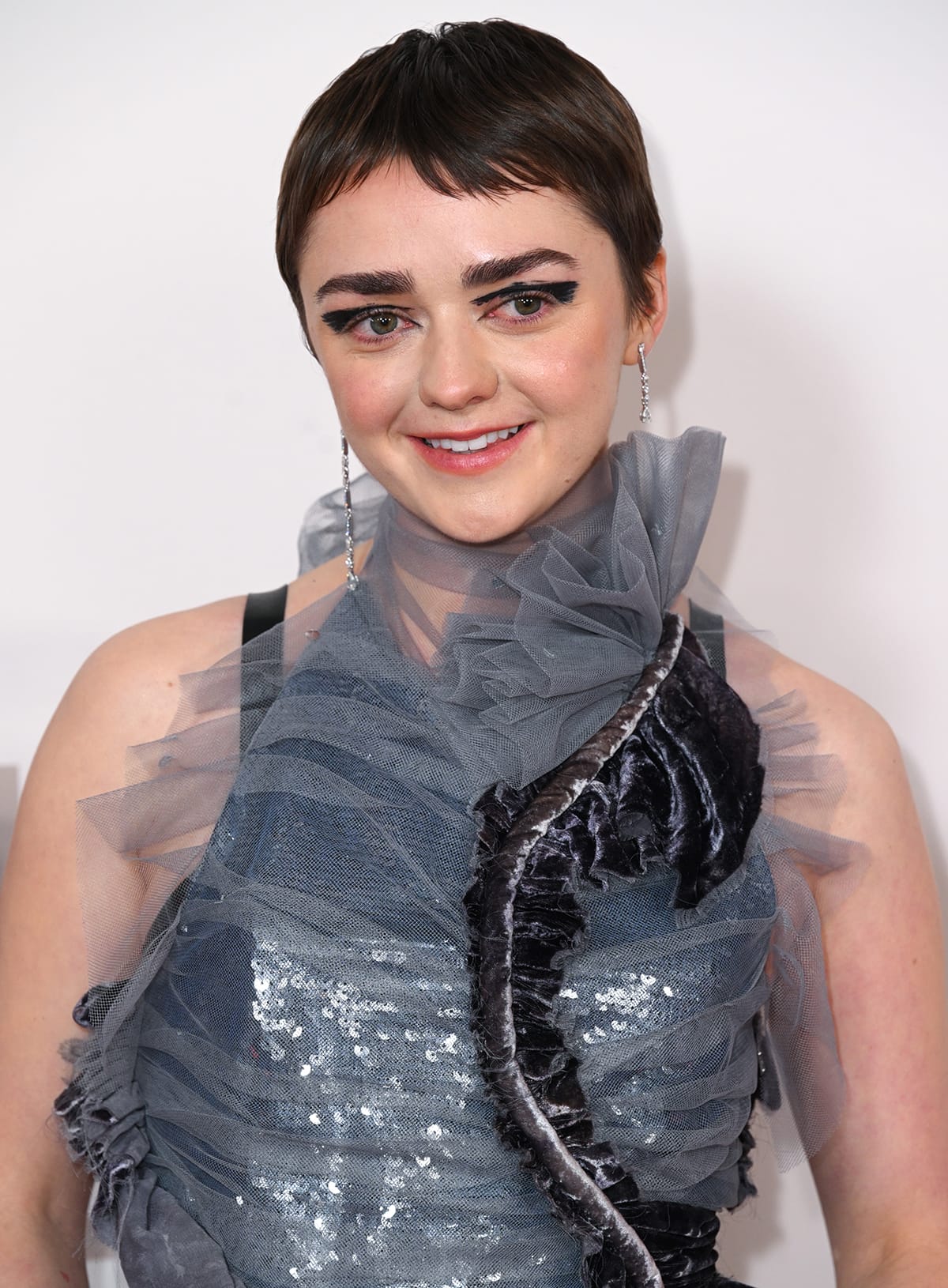 Maisie Williams rocks her glossy pixie haircut and wears theatrical makeup with smokey abstract eyeshadow