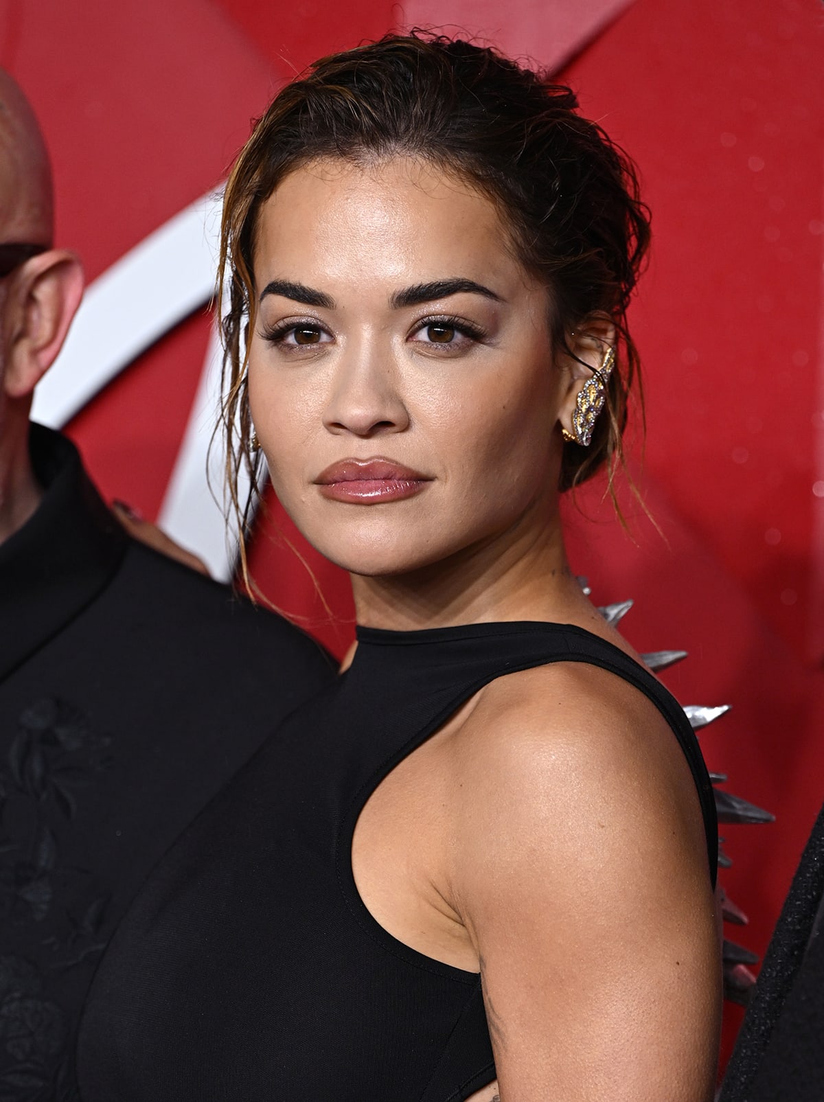 Rita Ora enhances her look with a messy updo, glittery eyeshadow, and mauve lipstick, adding to her glamorous appearance at the Fashion Awards 2023