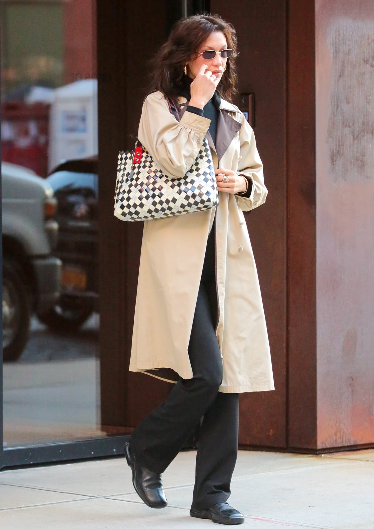 Transitioning to a minimalist era, Bella Hadid pairs a reversible two-toned trench coat with classic Prada boots, redefining street style with her unique flair