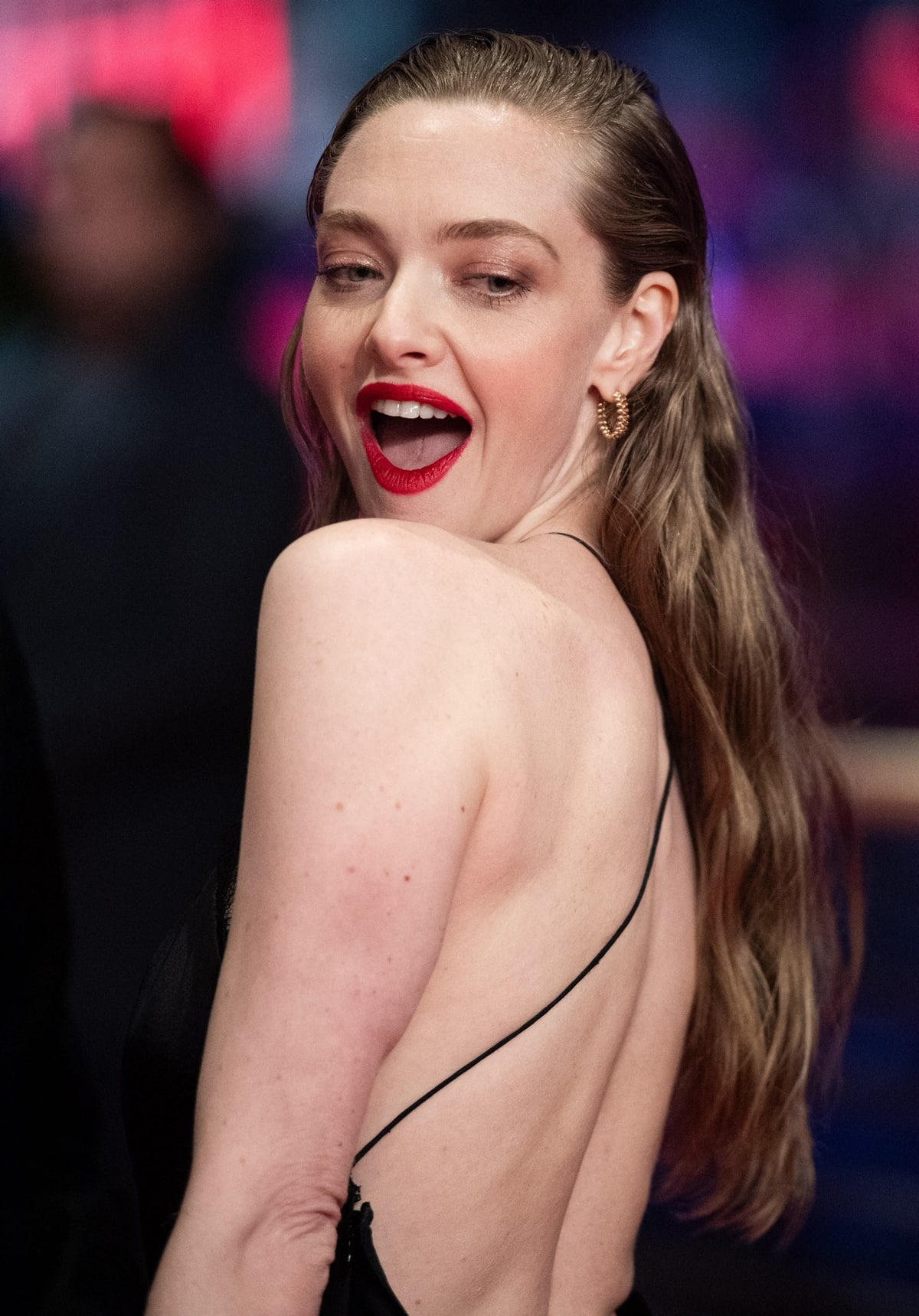 The backless design highlights Amanda Seyfried's sculpted back, while a halter neckline with intricate lace paneling adds elegance