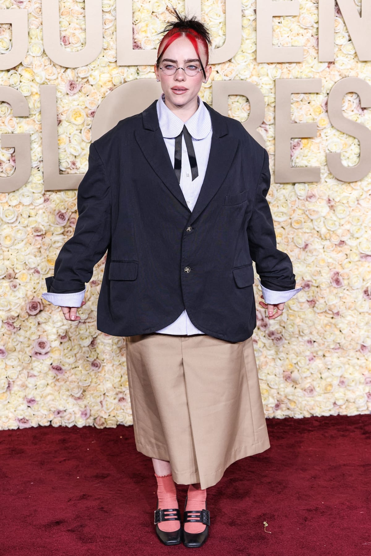 At the 2024 Golden Globe Awards, Billie Eilish showcased her unique style in an oversized black blazer, wide-leg khaki shorts, a blue and white pinstripe shirt with a black necktie from Willy Chavarria, and accessorized with Anita Ko diamond rings