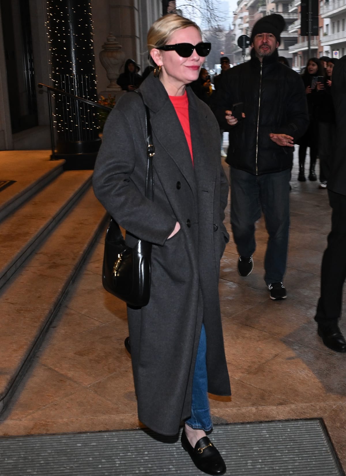 Dressed in a cozy crimson sweater tucked into navy wide-leg cropped jeans and layered with a long grey wool coat, Kirsten Dunst proves her fashion-forward sensibility
