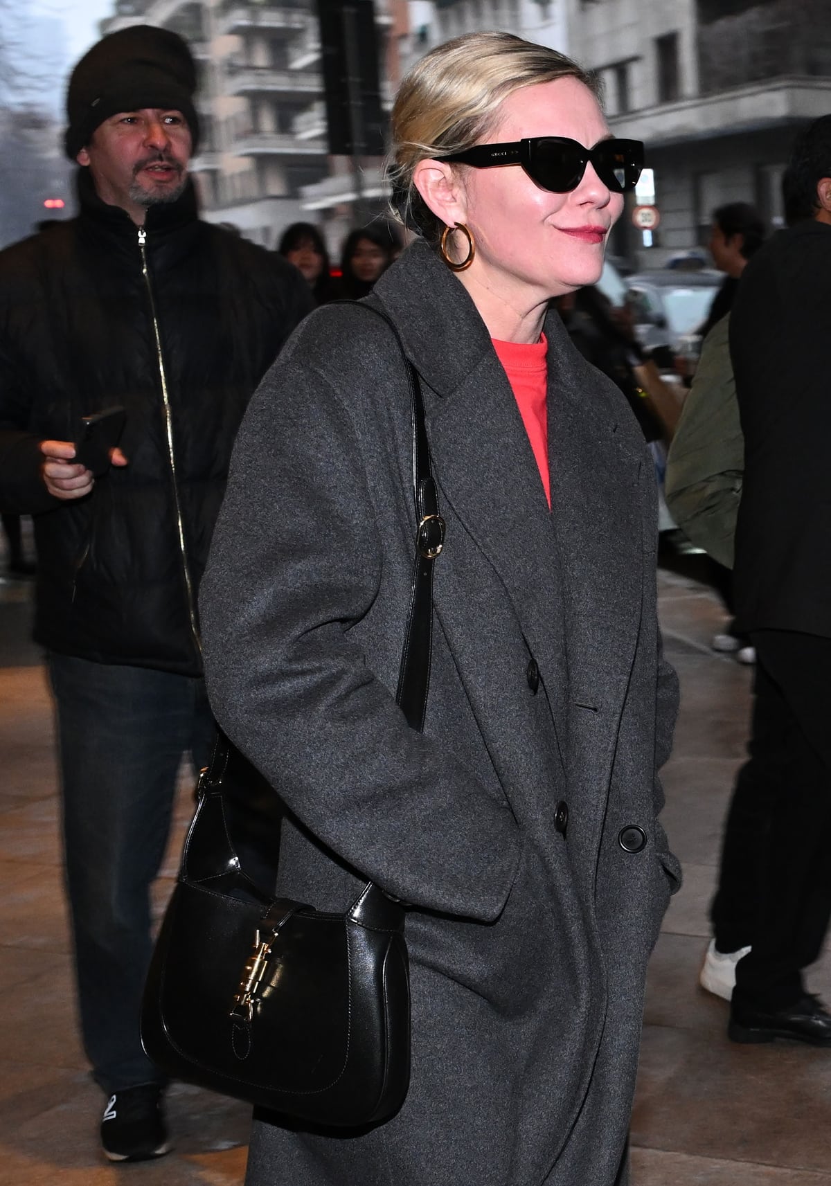 Completing Kirsten Dunst's outfit, a Gucci Jackie 1961 small shoulder bag, Gucci rectangular-frame sunglasses, and elegant gold hoop earrings, paired with her hair styled in an elegant updo, epitomize daytime chic