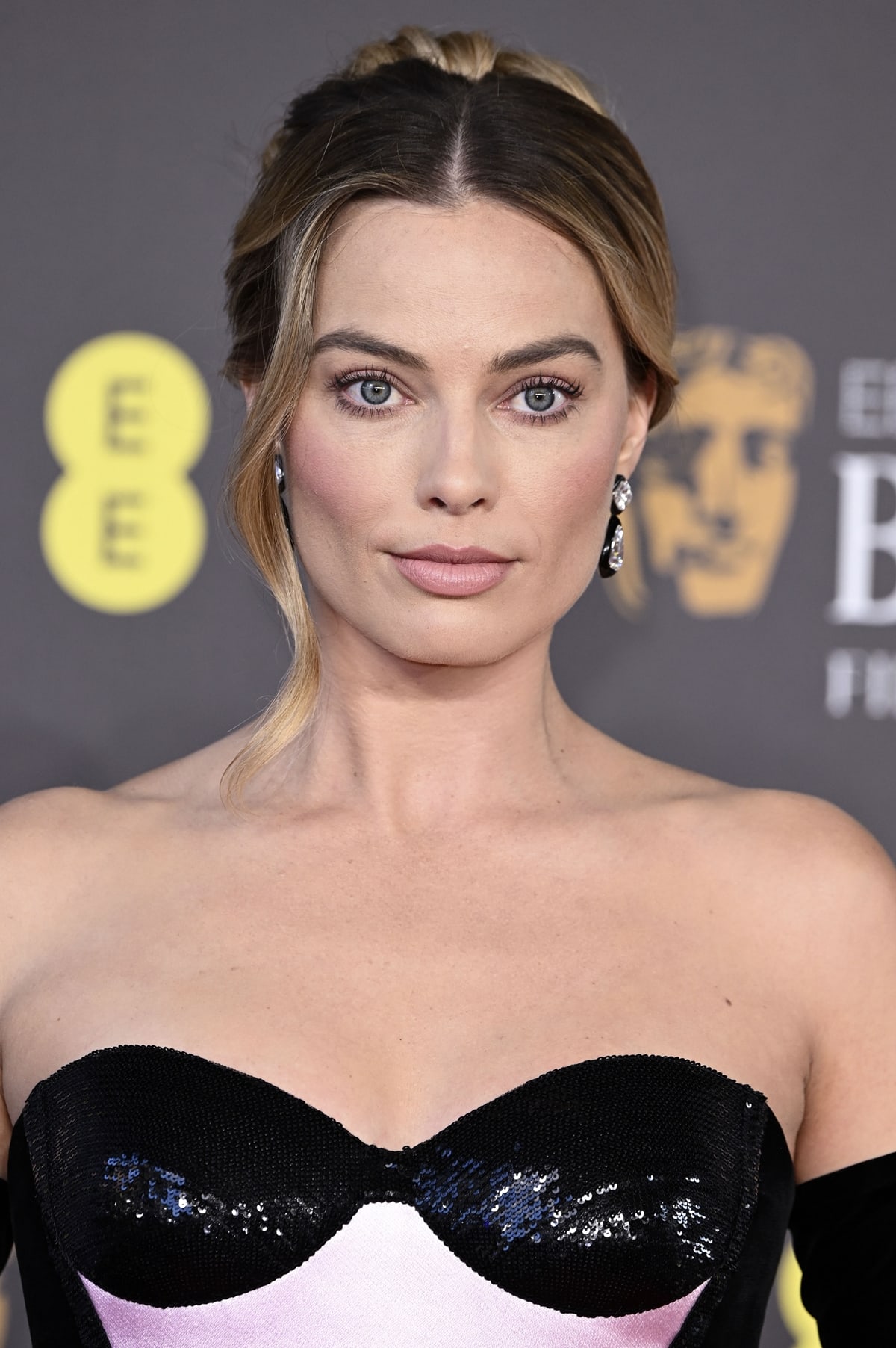 With black statement drop earrings, natural makeup with rosy cheeks, and a sophisticated updo, Margot Robbie's look for the 2024 BAFTA Film Awards is a masterclass in red-carpet elegance