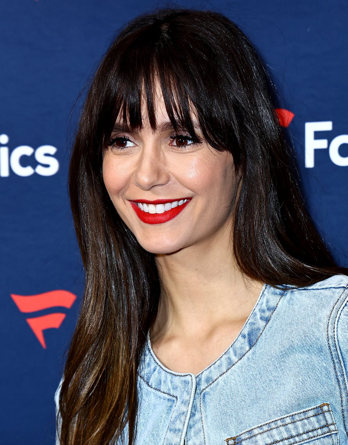 Nina Dobrev adds a pop of color to her double denim outfit by wearing bold red lipstick