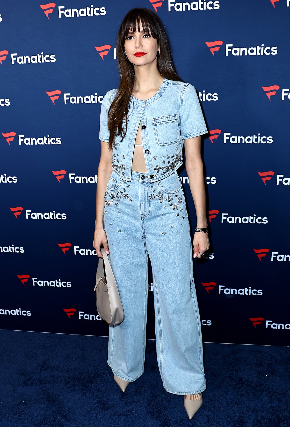 Nailing Canadian Tuxedo, Nina Dobrev attends Michael Rubin’s Fanatics Super Bowl 2024 Party in an embellished denim crop top and matching baggy jeans by Self-Portrait with taupe pumps and a By Far bag on February 10, 2024