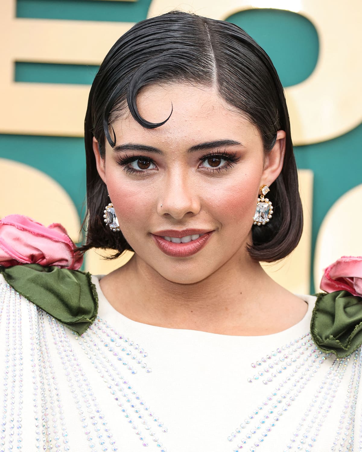 Xochitl Gomez glams up with rosy makeup and styles her short hair in a wet-look bob with kiss curls