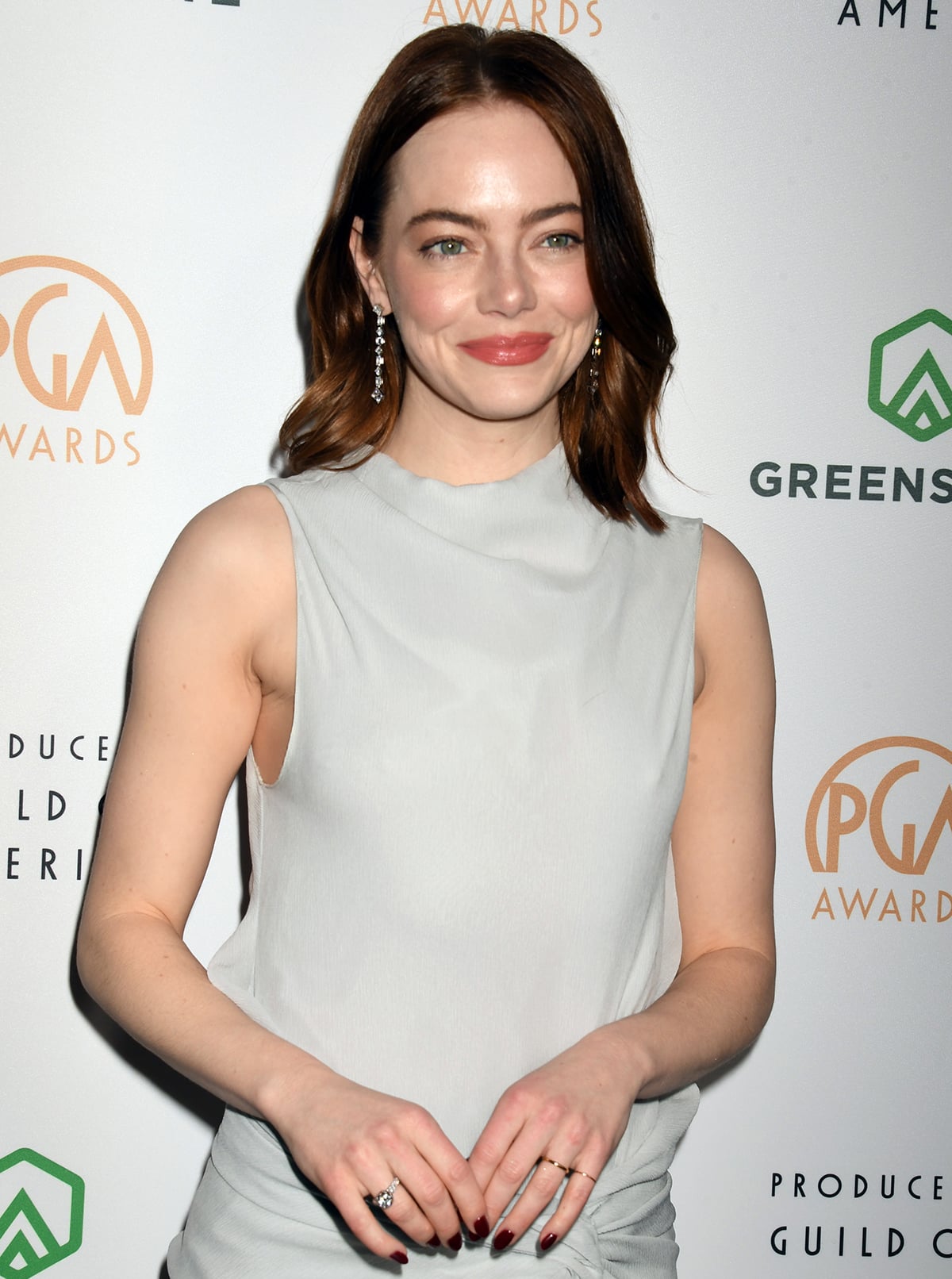 Emma Stone styles her muted gray look with sparkling dangling diamonds on her ears and a few rings on her manicured hands, all by Tiffany & Co.