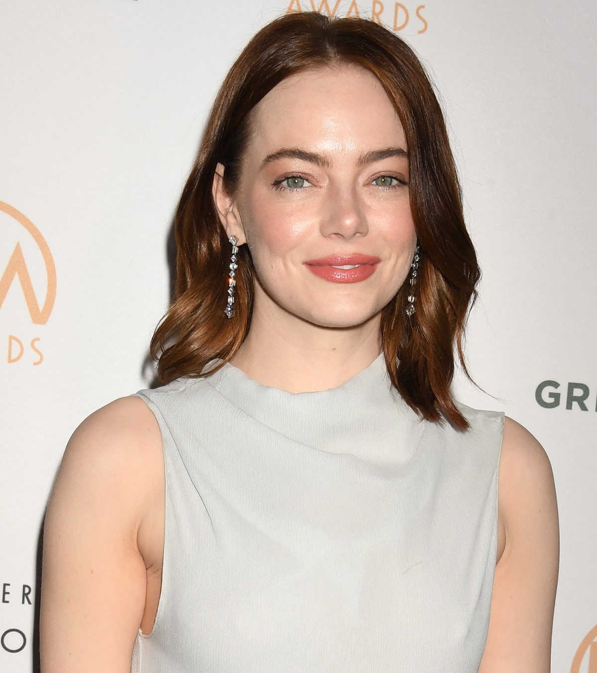Emma Stone opts for a radiant look with rosy cheeks and lips and styles her shoulder-length red hair in center-parted soft curls