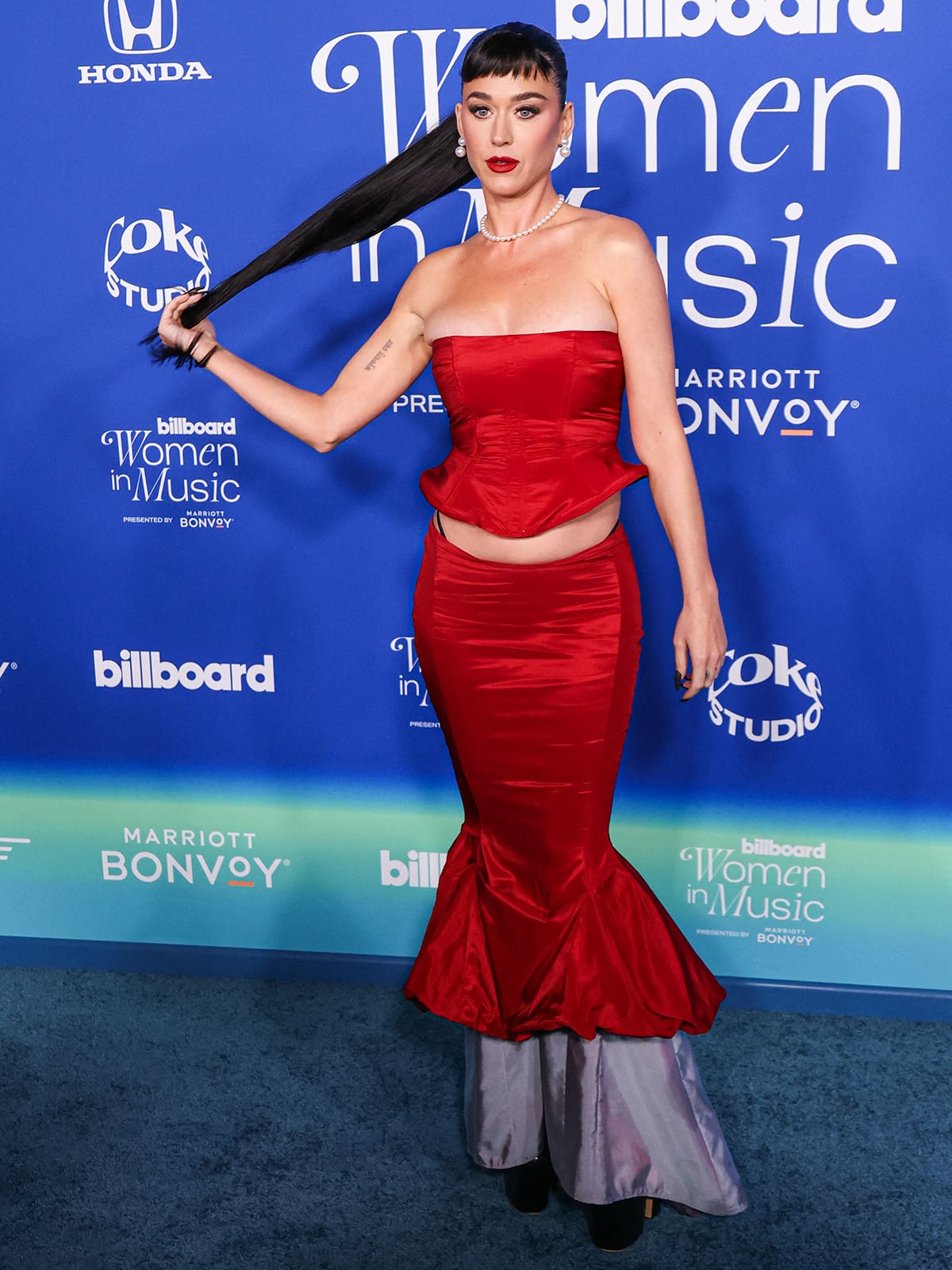 Katy Perry's red Ellie Misner outfit consists of a corset top and a mermaid skirt with a daring lace-up back