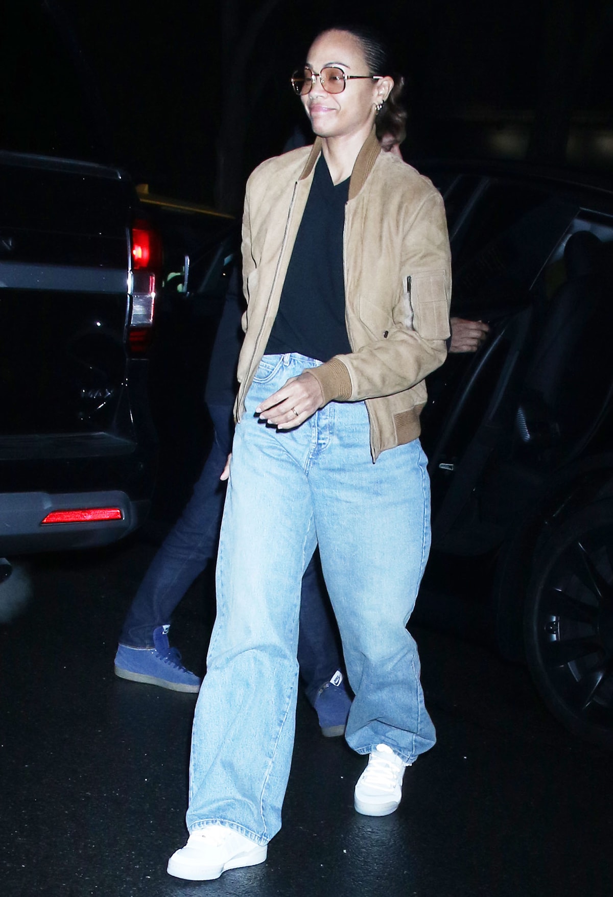 Zoe Saldana dresses casually in a black tee, baggy jeans, white sneakers, and a camel bomber jacket as she arrives at her Greenwich hotel on March 27, 2024