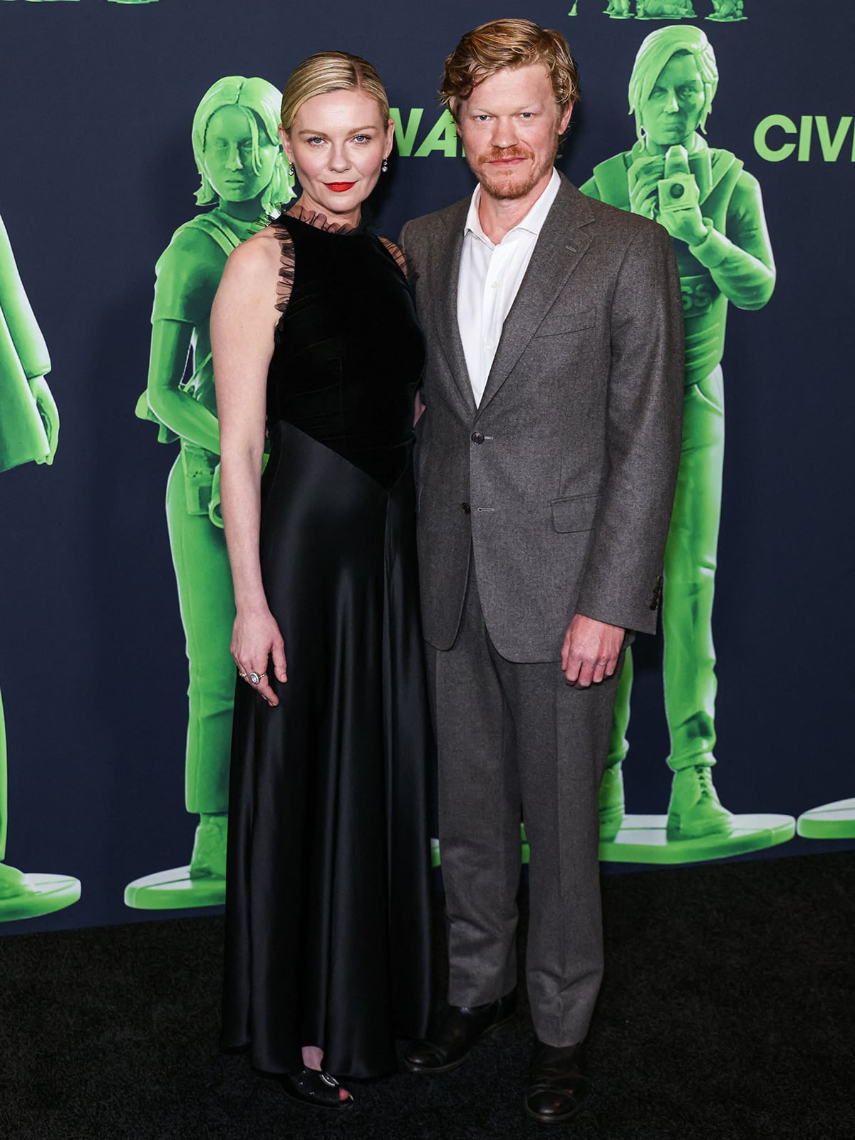 Kirsten Dunst is joined on the black carpet by her husband Jesse Plemons dressed in a gray suit, a white shirt, and black dress shoes 
