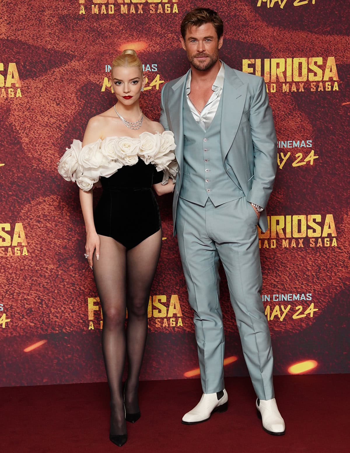 Anya Taylor-Joy, in a dramatic black bodice adorned with white roses, and Chris Hemsworth, dapper in a pastel blue suit, showcase their notable height difference at the "Furiosa: A Mad Max Saga" photocall in London