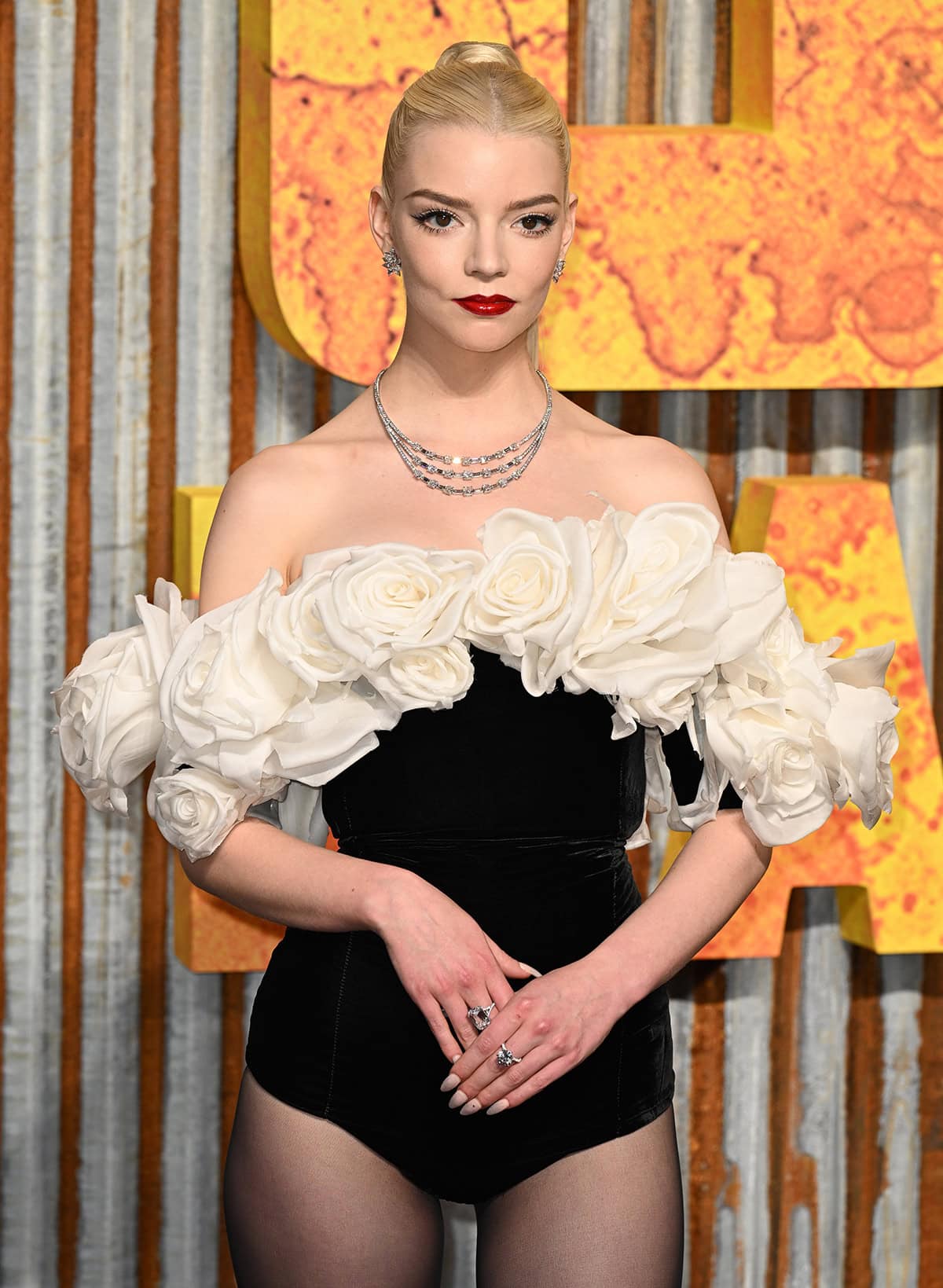 Anya Taylor-Joy styles her off-the-shoulder bodysuit with Tiffany & Co. jewelry, including a three-strand necklace, and wears vibrant red lipstick for a pop of color