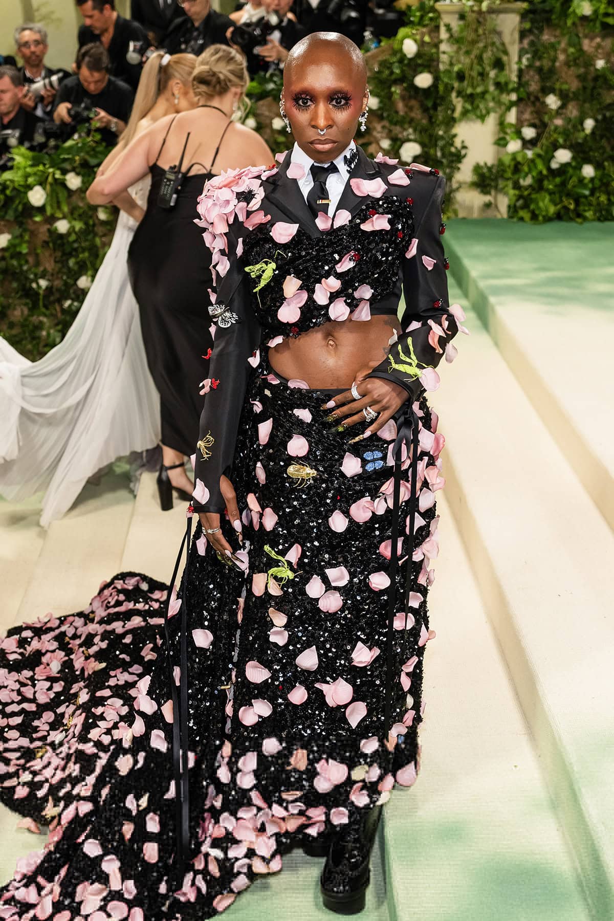 Cynthia Erivo radiates confidence in a custom Thom Browne ensemble featuring a cropped tuxedo jacket and a skirt overlaid with black sequins, lurex embroidery, pink silk petals, and 3D insects at the 2024 Met Gala